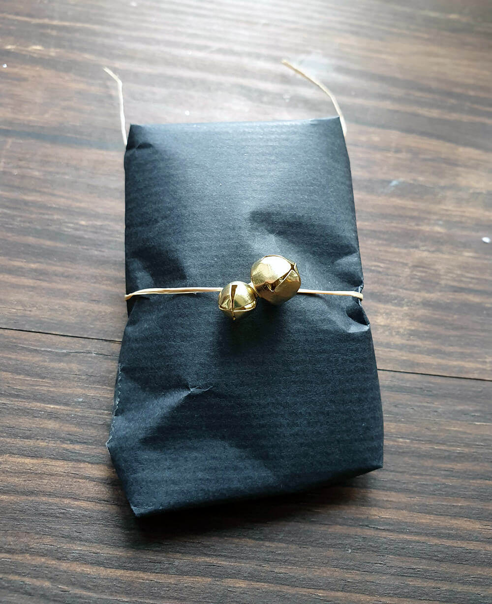 petit cadeau de noel emballé avec du papier kraft noir de la ficelle et des grelots - 7 idées d'emballage cadeau zéro déchet faciles à reproduire